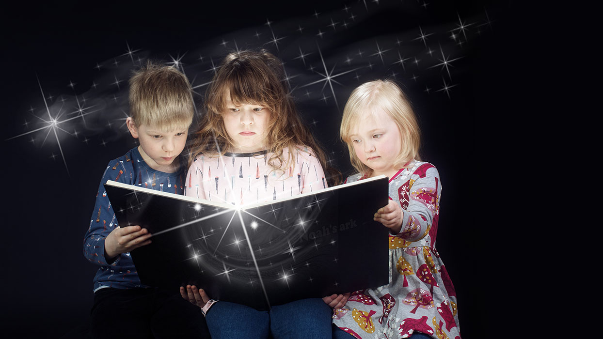Studiokuva: kolme lasta lukemassa hohtavaa kirjaa Valokuvaamo Datafunin studiossa